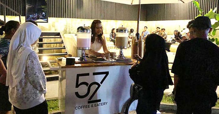 Suasana malam di 527 Café Serang dengan pengunjung mengantri di booth minuman bertuliskan “52/7 Coffee & Eatery”, mencerminkan suasana santai dan ramai yang direkomendasikan oleh Dream Home Specialist The Hana Park.