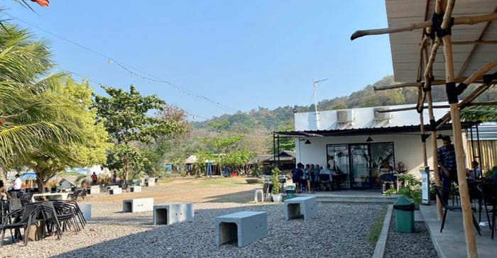 Area outdoor Tepian Café di The Hana Park dengan pemandangan pegunungan, tempat duduk terbuka, dan suasana santai yang cocok untuk bersantai bersama keluarga atau teman.