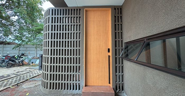 Pintu utama rumah The Hana Park dengan dinding roster untuk sirkulasi udara dan privasi area masuk